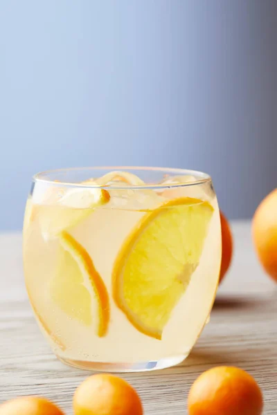 Close-up shot of glass of fresh lemonade with ripe oranges on wooden surface — Stock Photo