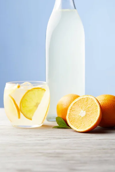 Vetro e bottiglia di limonata arancione con arance mature sul tavolo di legno — Foto stock