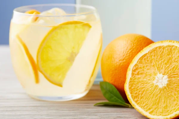 Vaso de limonada fría con naranjas maduras sobre mesa de madera - foto de stock