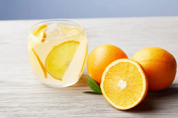 Vaso de refrescante limonada con naranjas maduras sobre mesa de madera - foto de stock