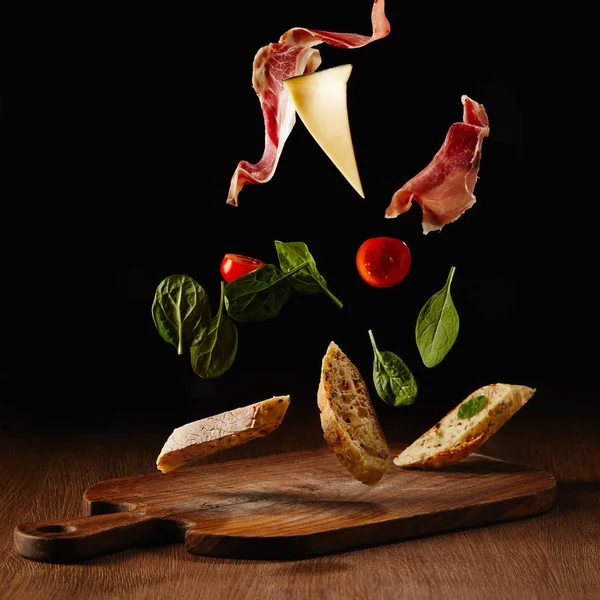 Ensalada fresca con jamón y queso para sándwich que cae sobre tabla de cortar de madera - foto de stock