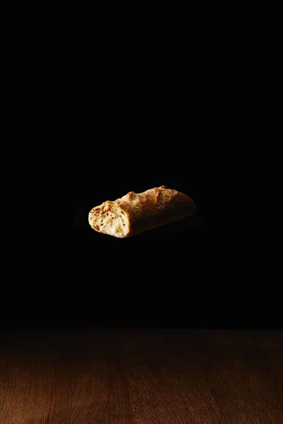 Piece of wholegrain bread flying above wooden table surface — Stock Photo