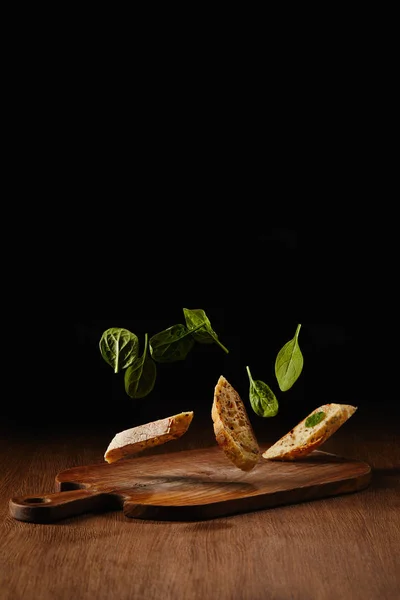 Bread pieces and salad leaves flying above wooden cutting board — Stock Photo