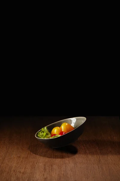 Tigela com tomates e folhas de salada em mesa de madeira — Fotografia de Stock