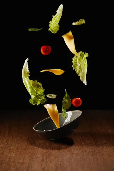 Ensalada fresca con rodajas de queso y bol volando sobre la superficie de la mesa de madera - foto de stock