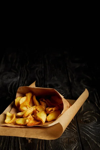 Golden french fries in craft paper on wooden table — Stock Photo