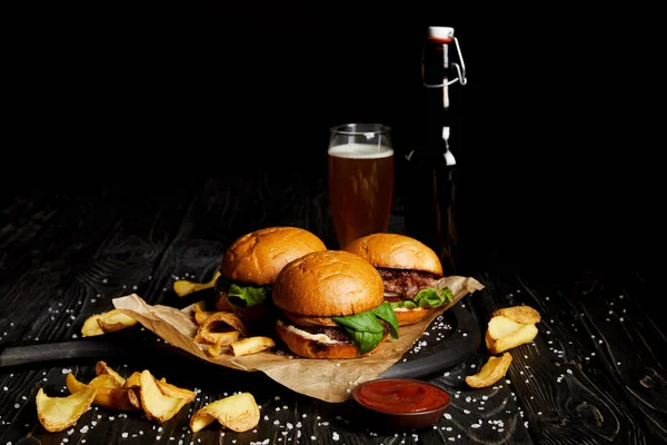 Set of junk food with burgers and french fries on table with beer in bottle and glass — Stock Photo