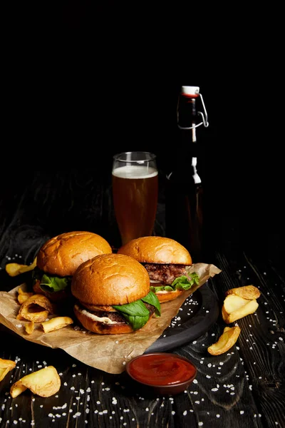 Tempting fast food hamburgers and french fries on table with beer in bottle and glass — Stock Photo