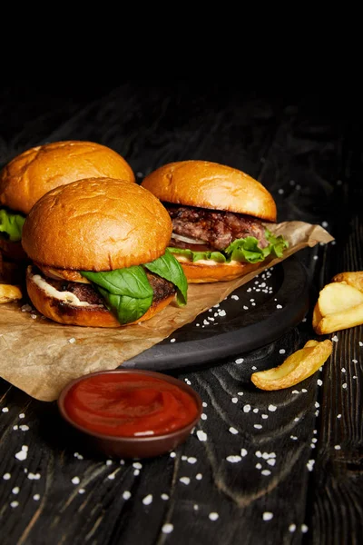 Hamburguesas y papas fritas con sal dispersa sobre mesa de madera - foto de stock