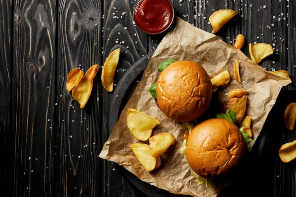 Vista superior de tentadoras hamburguesas de comida rápida y papas doradas sobre papel artesanal - foto de stock