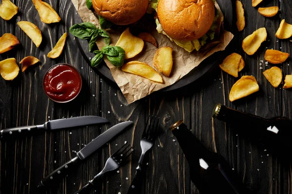 Hamburger und Pommes mit Bierflaschen und Besteck auf Holztisch — Stockfoto