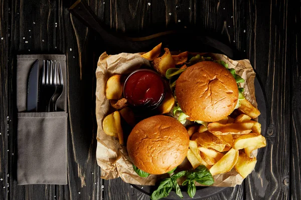 Hamburgers and french fries served on board by cutlery set — Stock Photo