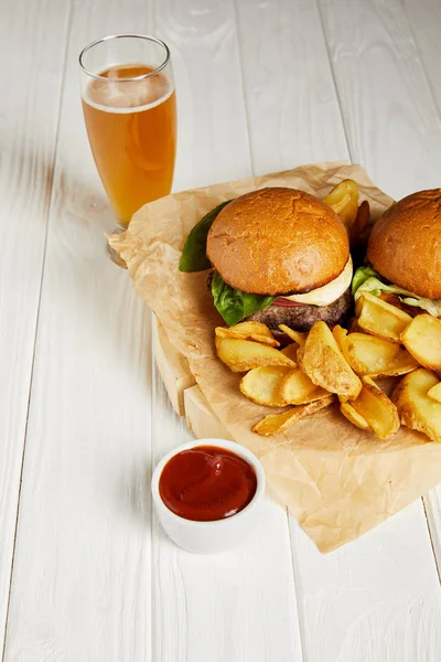 Conjunto de hamburguesas de comida chatarra y papas fritas servidas con cerveza sobre mesa blanca - foto de stock