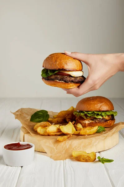Mão feminina segurando hambúrguer sobre jantar conjunto com batatas fritas — Fotografia de Stock