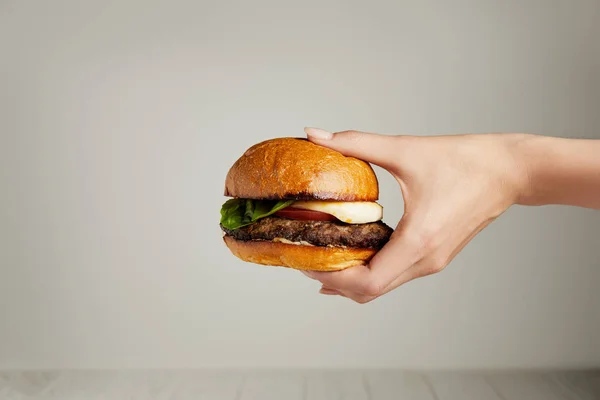 Hamburger chaud savoureux à la main féminine sur fond gris — Photo de stock