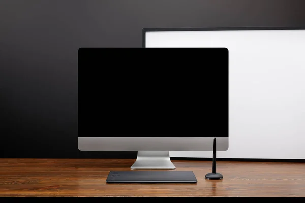 Закрытый вид на дизайнерское рабочее место с затемненным экраном компьютера и графической табличкой на деревянной столешнице — стоковое фото