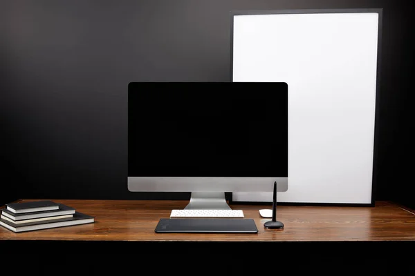 Vista de primer plano del lugar de trabajo del diseñador gráfico con tableta gráfica, pantalla de computadora en blanco, cuadernos y pizarra blanca vacía en la mesa de madera - foto de stock