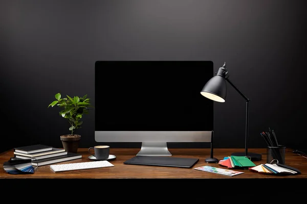 Vista de primer plano del lugar de trabajo del diseñador gráfico con tableta gráfica, pantalla de computadora en blanco, cuadernos y paleta en la mesa de madera - foto de stock