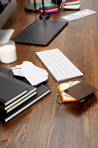 Close up view of graphic designer workplace with colorful pallet, notebooks and glass of milk on wooden surface — Stock Photo