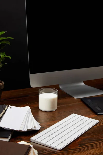 Close up view of designer workplace with glass of milk, computer screen and keyboard on wooden tabletop — Stock Photo