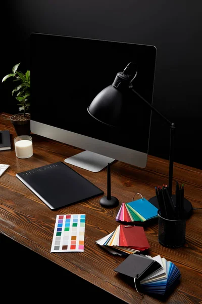 Крупный план графического дизайнера рабочего места с красочным поддоном, графическим планшетом, чистым экраном компьютера и лампой на деревянной поверхности — стоковое фото