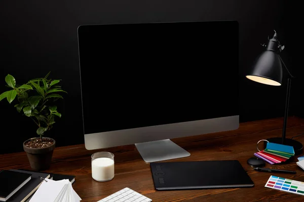 Крупный план графического дизайнерского рабочего места с красочным поддоном, чистым экраном компьютера, лампой и графическим планшетом на деревянной поверхности — стоковое фото