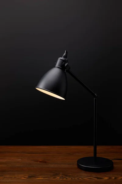 Close up view of black lamp on wooden tabletop on black background — Stock Photo