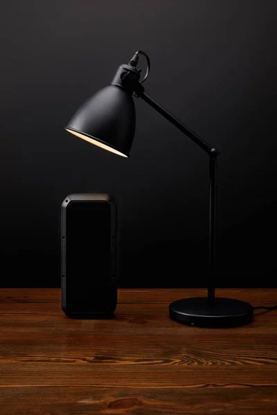 Vue rapprochée du haut-parleur audio noir et de la lampe sur une surface en bois sur fond de mur noir — Photo de stock