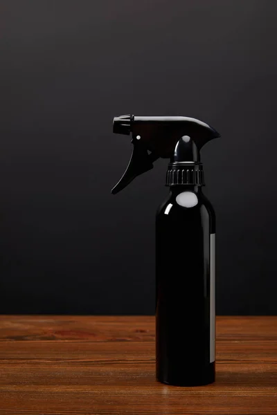 Close up view of black spray bottle on wooden surface on black wall background — Stock Photo