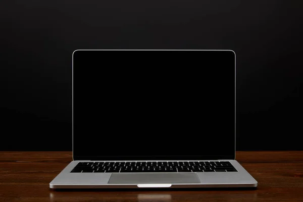Vista de cerca de la computadora portátil con pantalla en blanco en la mesa de madera sobre fondo de pared negro - foto de stock