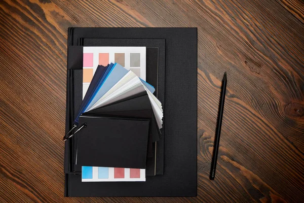 Flache Lage mit schwarzen Notizbüchern, Farbpalette und Bleistift auf Holztischplatte — Stockfoto