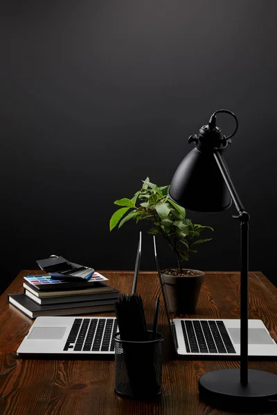 Vue rapprochée du lieu de travail du designer avec des ordinateurs portables, des ordinateurs portables et des palettes sur table en bois sur fond de mur noir — Photo de stock