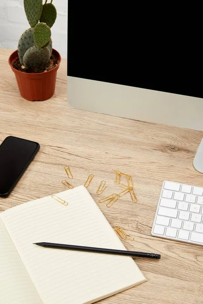 Nahaufnahme des Designerarbeitsplatzes mit Smartphone, Notebook, Computerbildschirm und Tastatur auf Holzoberfläche — Stockfoto