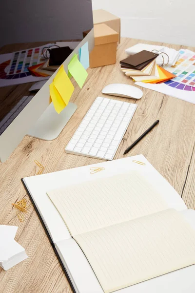 Vue rapprochée du lieu de travail du designer avec écran d'ordinateur avec autocollants colorés, cahiers et palette sur table en bois — Photo de stock