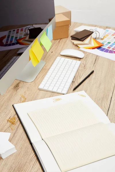 Close up view of designer workplace with computer screen with colorful stickers, notebooks and pallet on wooden tabletop — Stock Photo