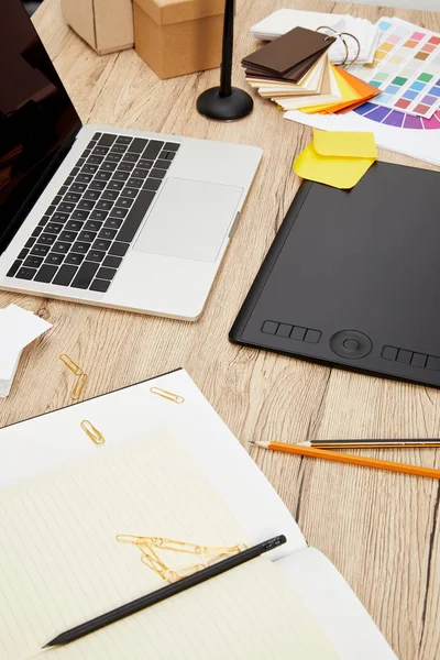 Крупный план ноутбука, графического планшета, ноутбуков и поддонов на деревянной поверхности на графическом дизайнерском рабочем месте — стоковое фото