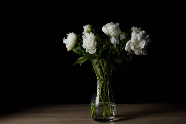 Beautiful white peonies in glass vase on wooden table and on black — Stock Photo