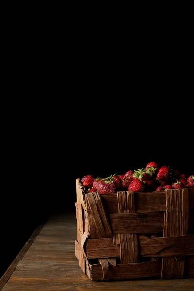 Fraises mûres fraîchement récoltées en boîte rustique sur fond noir — Photo de stock