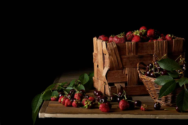 Ciliegie e fragole appena raccolte su tavolo di legno e su nero — Foto stock