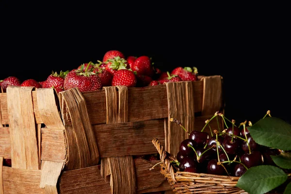 Спелые вишни и клубника в корзине и коробке изолированы на черном — стоковое фото