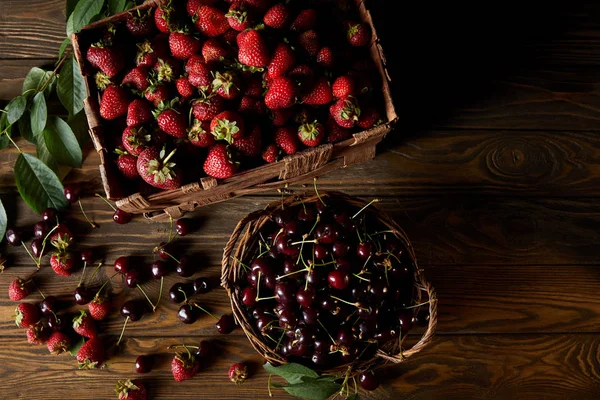 Vue de dessus des cerises et des fraises dans le panier et la boîte sur le dessus de table en bois — Photo de stock