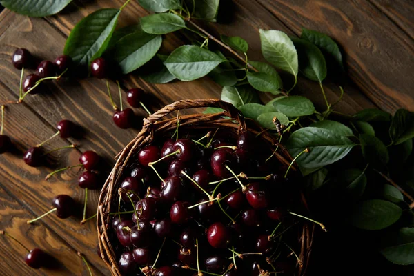 Сверху вид на свежие красные сладкие вишни в деревенской корзине на деревянном столе с листьями — стоковое фото