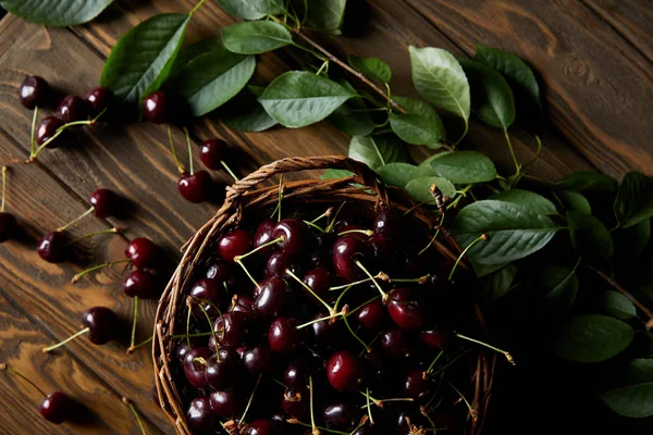 Vue de dessus de cerises douces rouges fraîches dans un panier rustique sur une table en bois avec des feuilles — Photo de stock