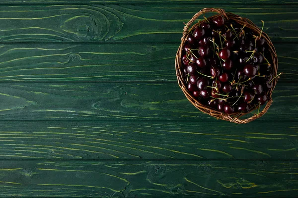 Vue de dessus des cerises fraîches dans le panier sur la surface en bois vert — Photo de stock