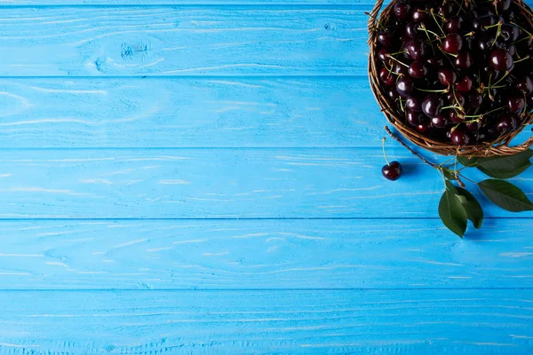 Draufsicht auf rote Kirschen im Korb auf blauer Holzoberfläche — Stockfoto