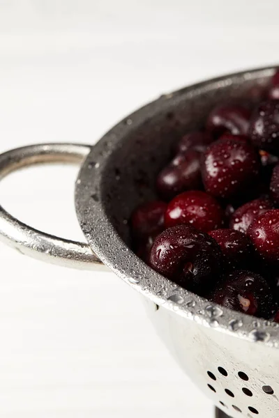 Gros plan de cerises fraîches mûres en passoire métallique sur plateau blanc — Photo de stock