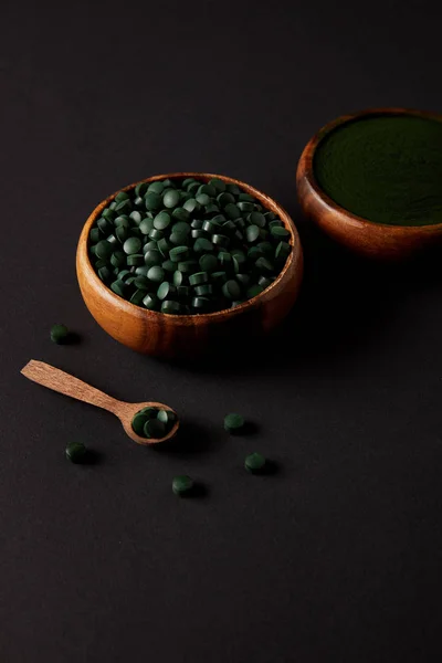 Cucchiaio di legno e ciotole con Spirulina macinata e Spirulina in pillole sul tavolo grigio — Foto stock