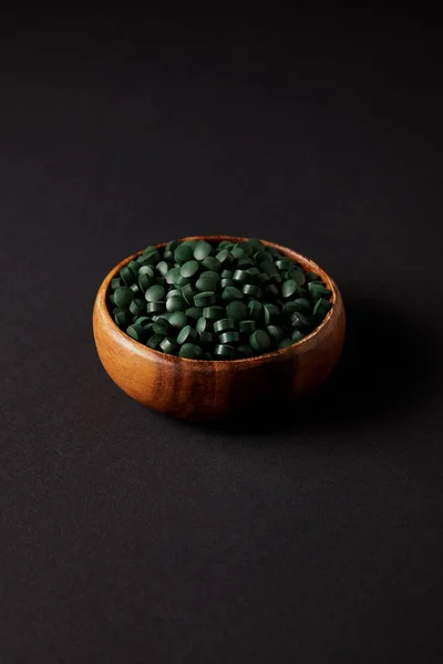 Tigela de madeira com pilha de pílulas spirulina na mesa cinza — Fotografia de Stock