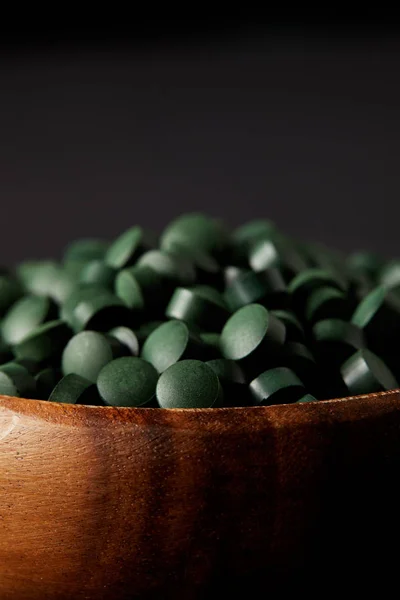 Vista de perto de tigela de madeira com pilha de pílulas spirulina isolado em fundo cinza — Fotografia de Stock