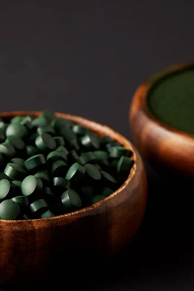 Selective focus of wooden bowls with spirulina powder and spirulina in pills on grey background — Stock Photo